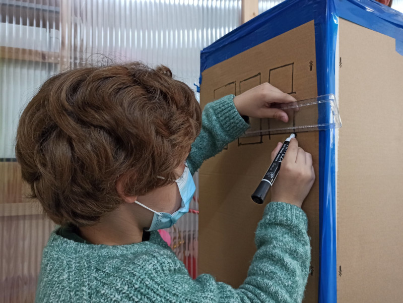 Un niño haciendo ventanas en cartón con una regla